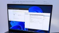 Windows 11 displaying BitLocker settings on a laptop in front of a BitLocker Drive Encryption page from Microsoft