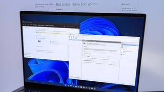 Windows 11 displaying BitLocker settings on a laptop in front of a BitLocker Drive Encryption page from Microsoft