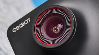 a black small 4K webcam with a red button photographed on a beige surface against a blue background