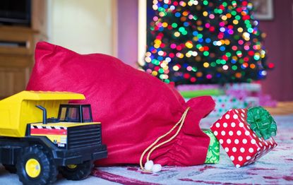 Red Santa christmas sacks next to a toy truck and by a Christmas tree