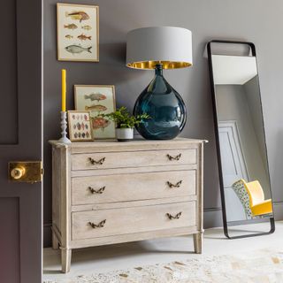 drawers with grey wall and table lamp with mirror
