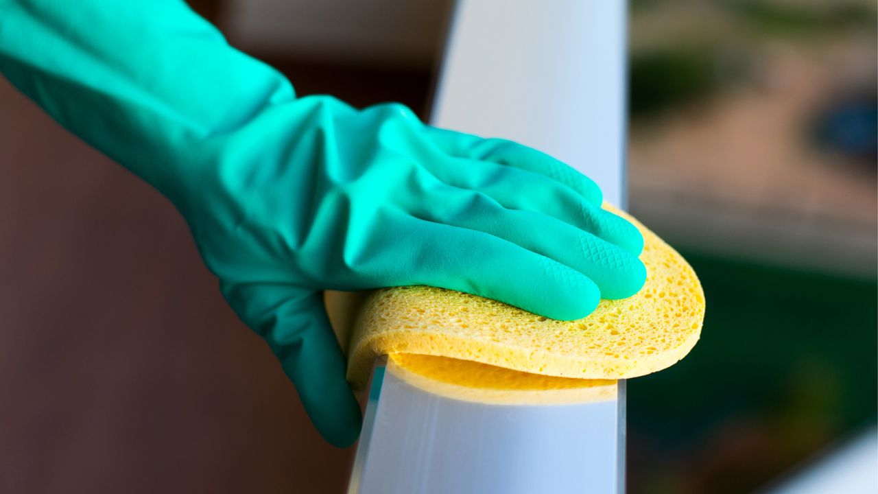 Person cleaning balcony railing with green cleaning glove and yellow sponge - for article on all the places you&#039;re probably forgetting to clean on your balcony