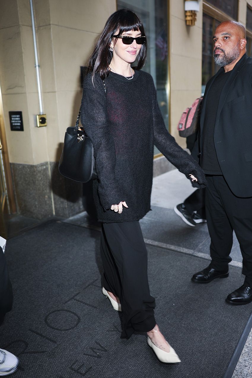 Dakota Johnson wearing a sheer black sweater, maxi skirt, and cream pointed-toe glove pumps in NYC
