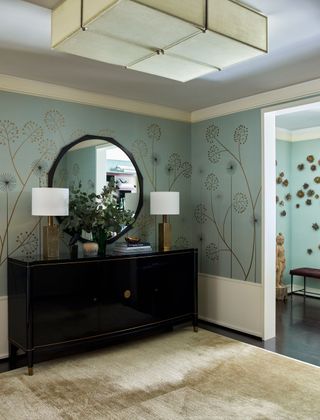 Entry foyer with jade floral wallcovering and buffet cabinet with round mirror and large rectangular ceiling light