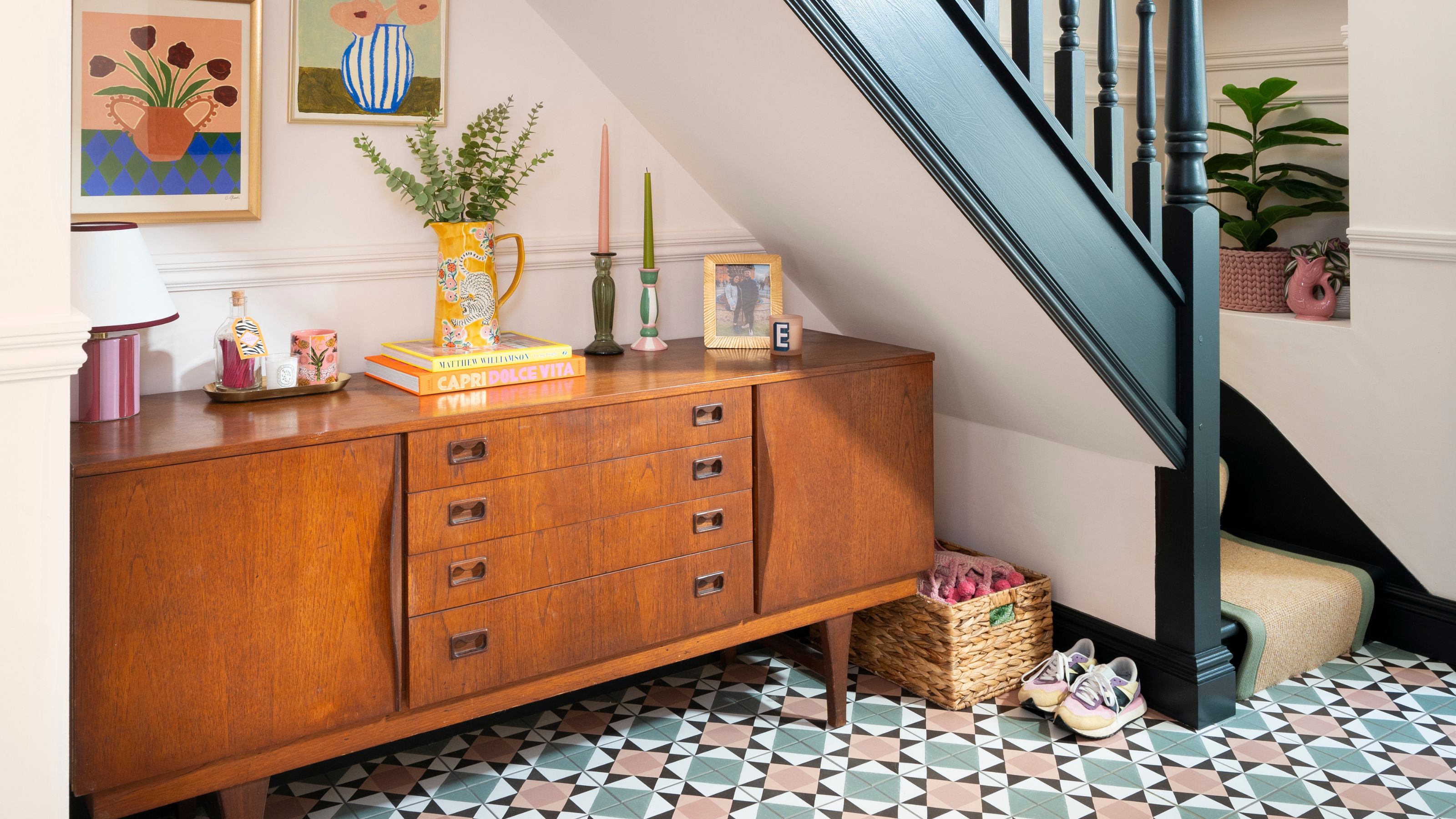 Hallway with colourful floor tiles and a wooden cabinet underneath the stairs