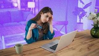 Woman sitting at table in front of laptop, looking annoyed and holding a credit card.