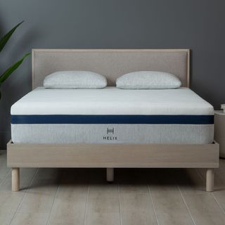 The Helix Midnight mattress for side sleepers placed on a light wooden and fabric bed frame in a grey bedroom