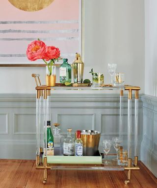 A kitchen corner decorated with a gold and perspex bar cart and a pink and silver wall art