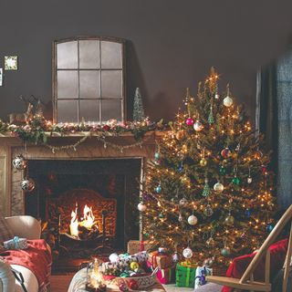 A decorated Christmas tree with Christmas lights in a living room next to a lit fireplace