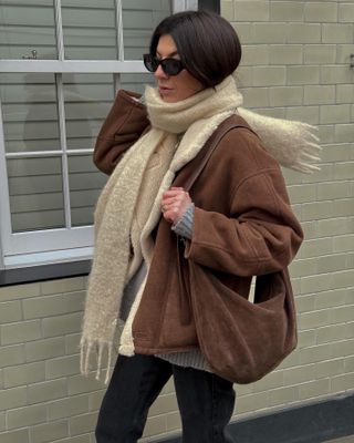 Woman wears brown jacket, brown bag, cream scarf