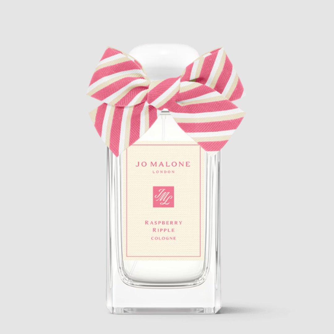 A product shot of the Jo Malone Raspberry Ripple cologne, which features a pink and cream bow on its lid, on a grey background