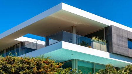 Corner of an ultra modern house in Portugal with large terrace and glass railing against a blue sky