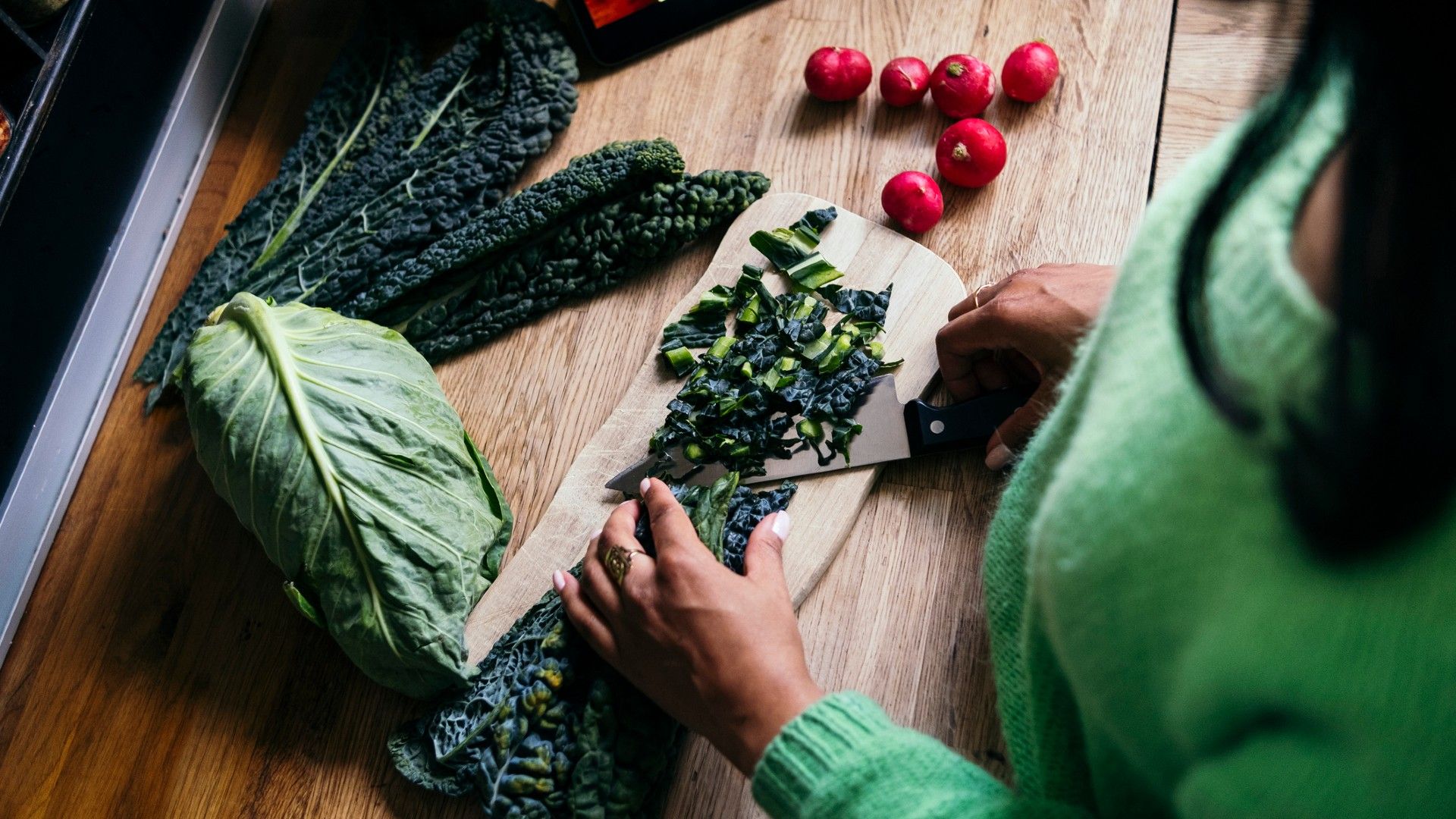 woman chopping up leafy greens on kitchen countertop, with radishes to the right to show things you shouldn't put in a microwave
