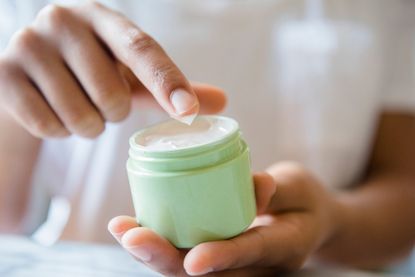 A close-up of a woman's hands holding a pot of cream like magnesium butter