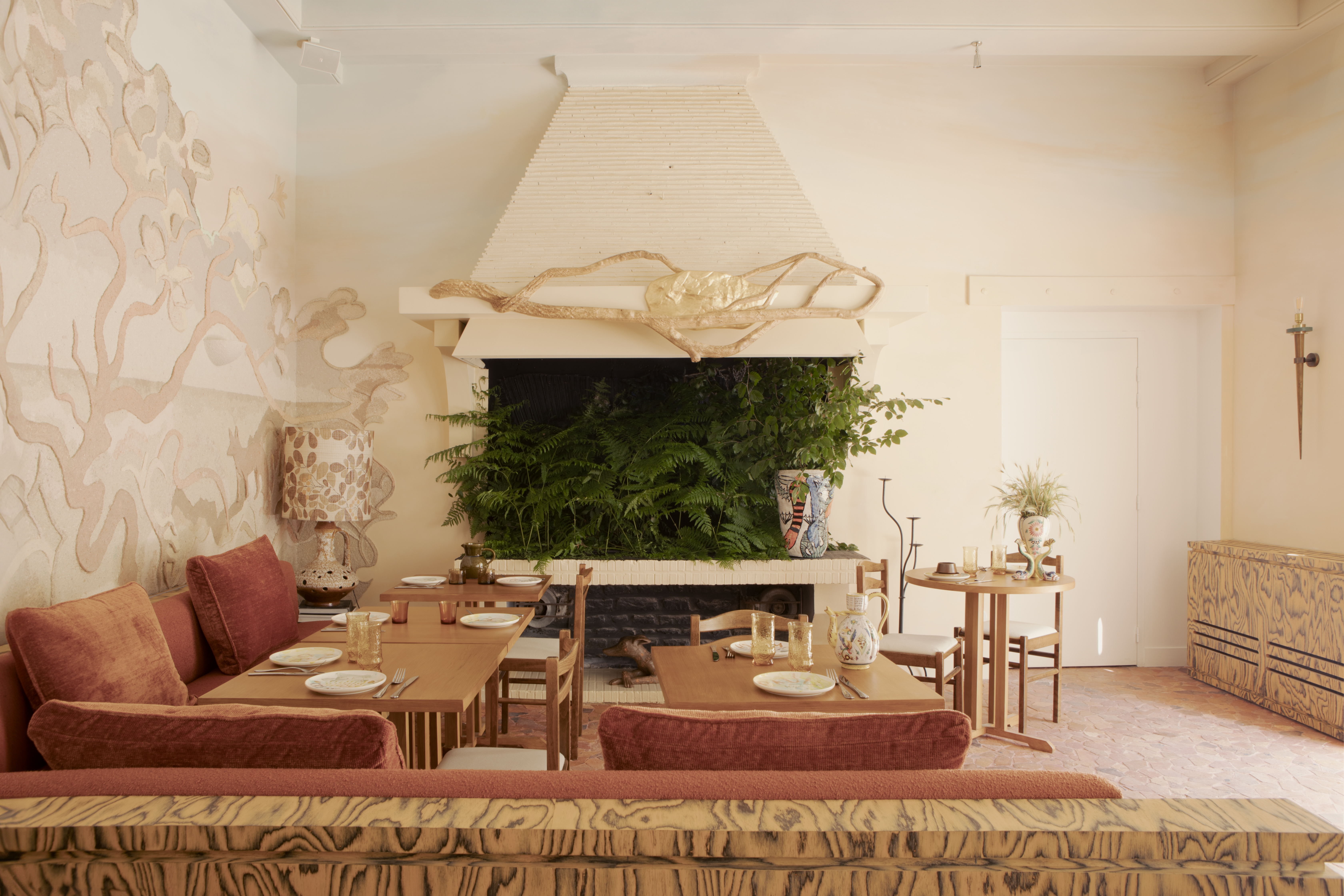 A whimsically designed hotel boasts richly layered interiors characterized by hand-drawn, fantastical mural motifs, earthy and pastel shades, and shapely furniture.
