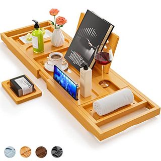 A wooden extending bath tray shelf with clutter on top. A book stand props a book standing up