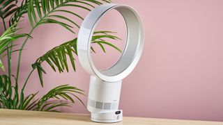 The Dyson Cool CF1 is shown tilted downwards while sitting on a tabletop, in front of a leafy green plant.