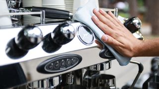 A hand wiping down the front of a stainless steel espresso machine