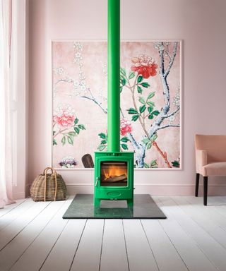 Bright green stove in pink living room with floral framed wallpaper, white painted wooden floorboards,