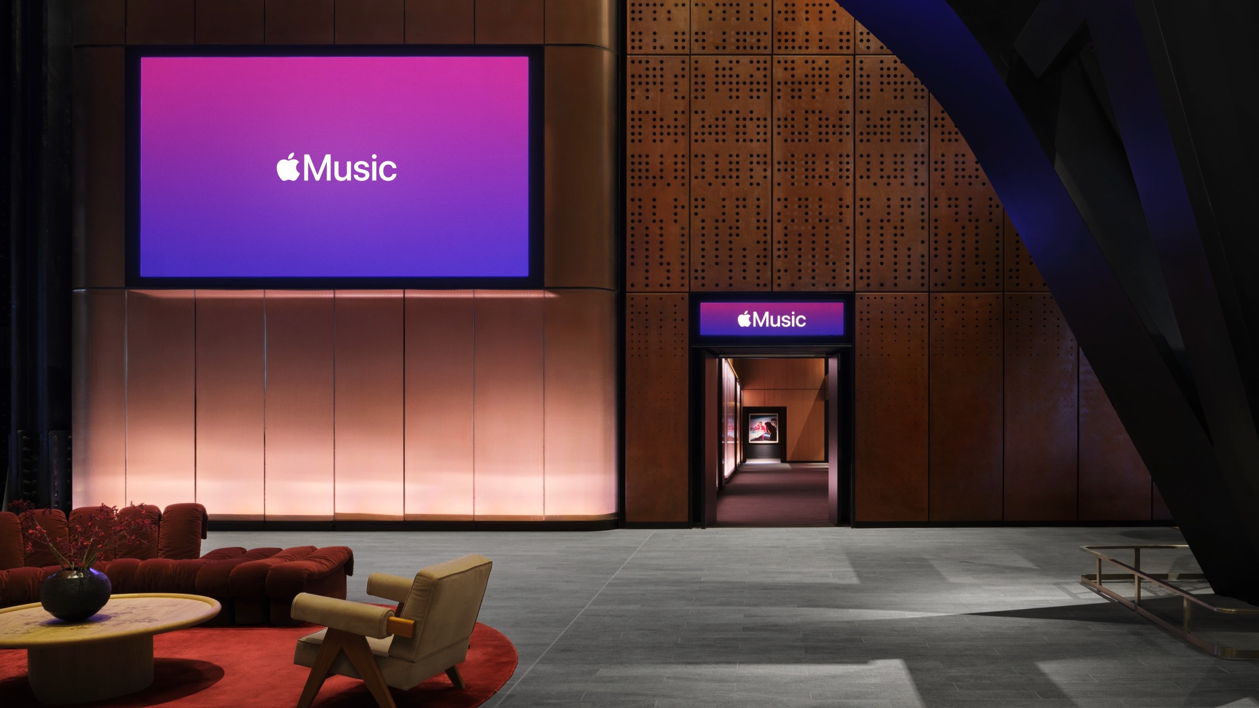 The foyer inside Apple Music Hall, with a sofa, armchair and Apple Music branding on a screen and above a door.
