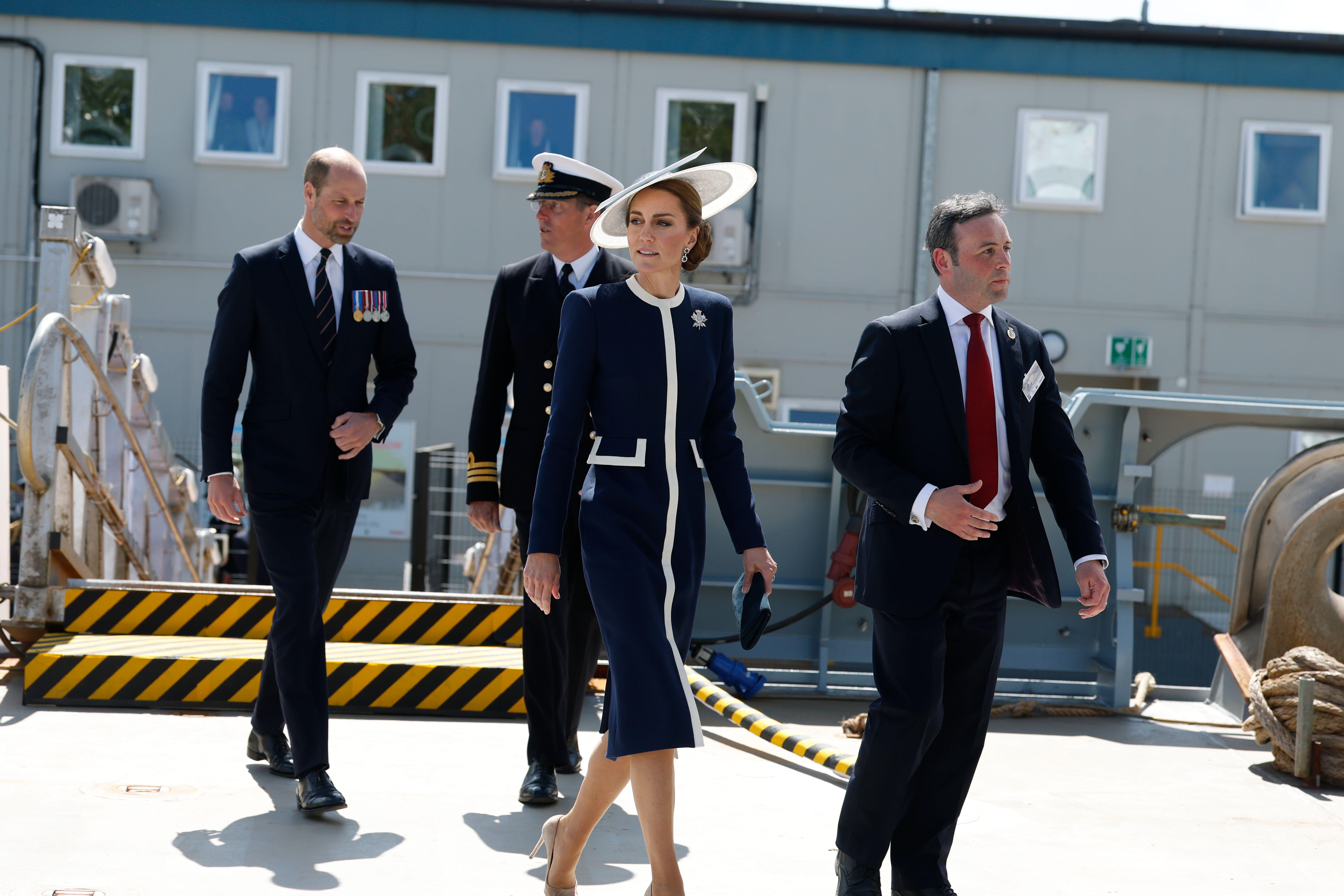 Kate Middleton walking in a navy and white coat with Prince William