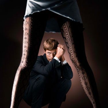 woman in short dress tights and high heels with man in a suit crouching behind her