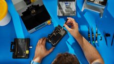 A person fixes an iPhone using one of Apple's Self Service Repair kits on a blue desk mat.