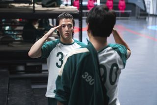 A man (Kang Ha-neul) salutes another man as they stand in the dormitory in 'Squid Game' season 2.