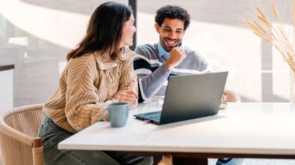 Young smiling couple calculating their finances at home on their laptop 