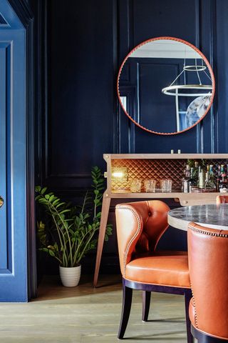 Dining room with dark blue panelled walls, leather dining chairs beside a marble topped table and bar