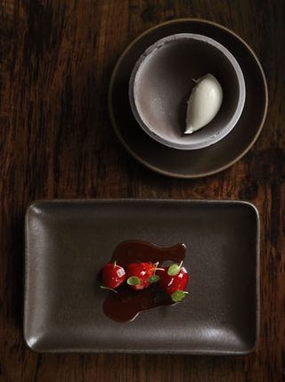 Close up of neatly presented dish of strawberry's on a dark brown dish, ice cream prsented in a dark brown dish, dark wood surface