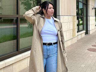 female fashion influencer Marina Torres poses with a butterfly clip up-do, statement earrings, basic white t-shirt, trench coat, black belt, and jeans