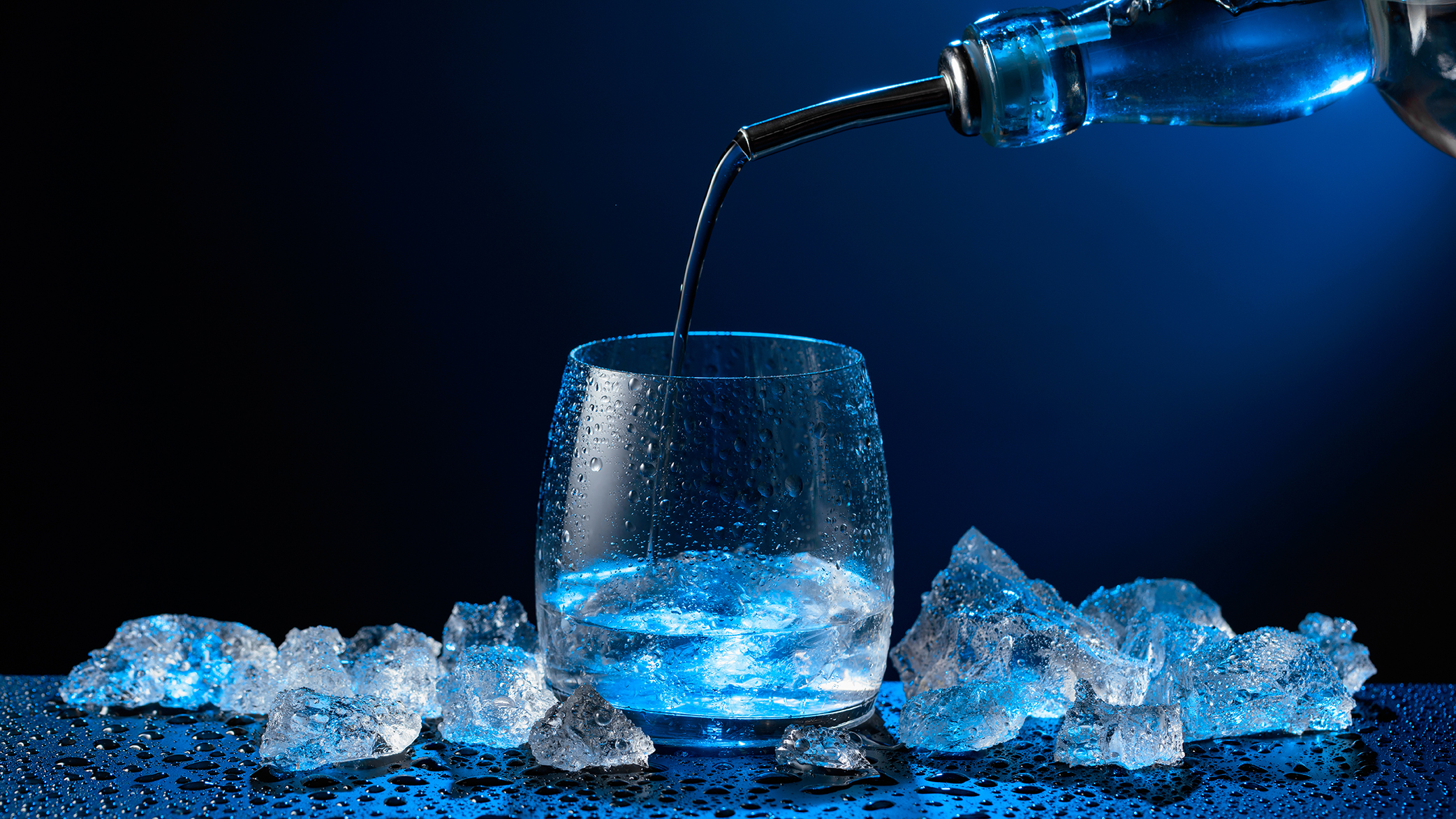 A spirit being poured into a glass surrounded by ice