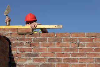 A bricklayer builds a wall with a blue sky in the backdrop