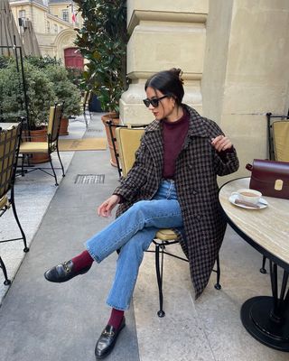 @leasy_inparis wears a burgundy jumper, a checked wool coat, jeans, burgundy socks and loafers