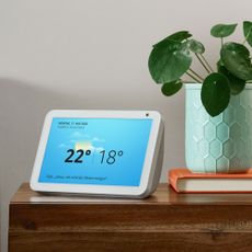 voice control smart speaker hub with screen on a sideboard showing the weather beside a potted plant