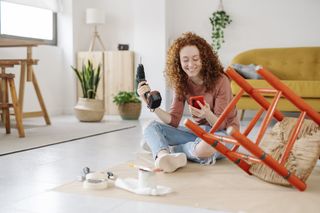 Woman using a mobile phone while renovating and repairing an old chair