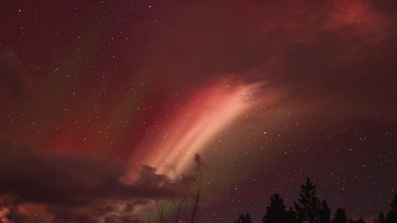 A red streak of STEVE shines between cloud cover.