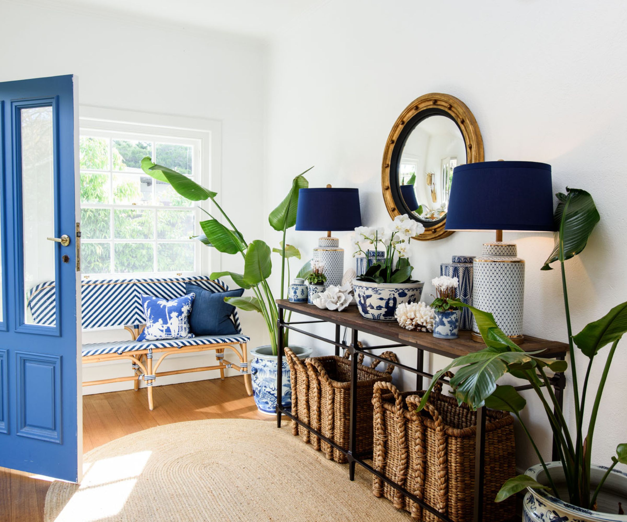 Entryway with rattan rug, rattan baskets, large blue table lamps, blue and white china and round mirror