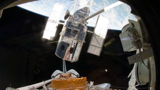 view of hubble with two solar panels above a space shuttle in space. the earth is behind. a robotic arm is between the shuttle and hubble