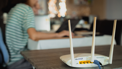 A woman works in the background, a broadband router in the foreground