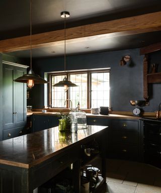 dark blue kitchen with beams, color drenched, small kitchen island, wooden and copper countertops, glassware, pendant lights, black oven, deVOL