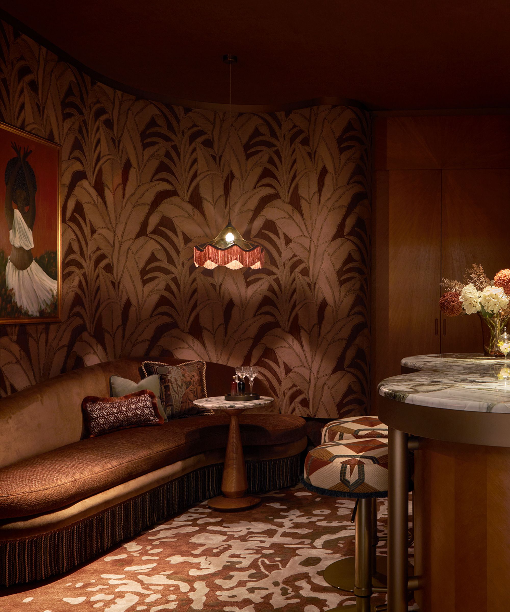 A moody home bar with brown floral wallpaper and art deco furnishings