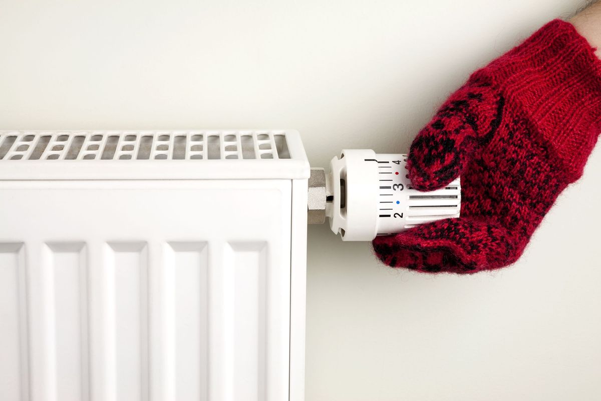 Person wearing a mitten adjusting a radiator thermostat.