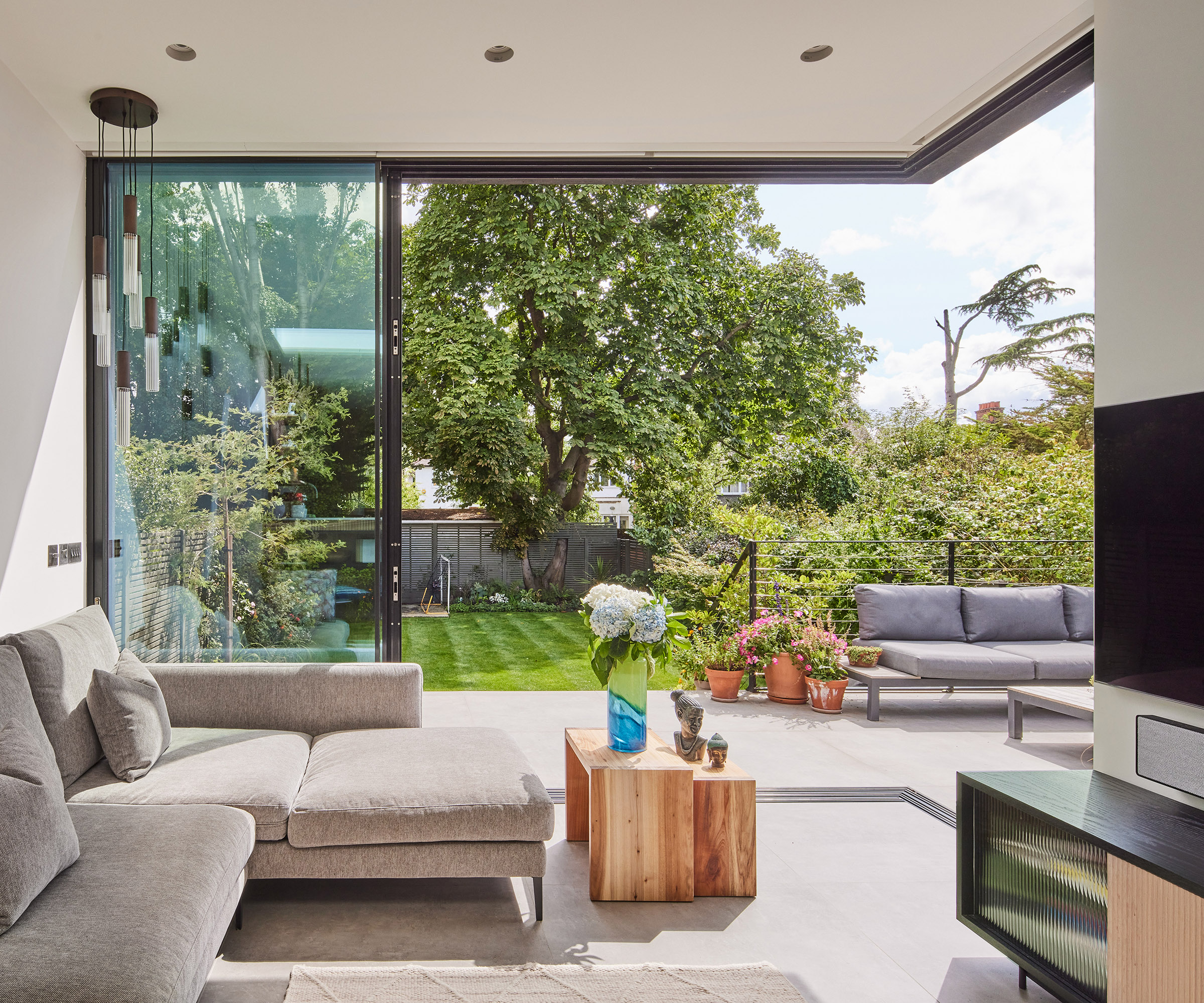 View of a cantilevered modern extension with open indoor/outdoor space with glass sliding doors out onto a patio