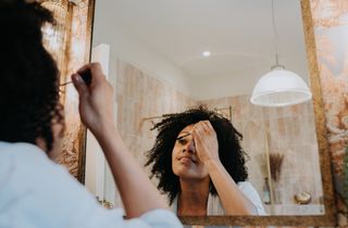 A lady putting on makeup in the mirror.