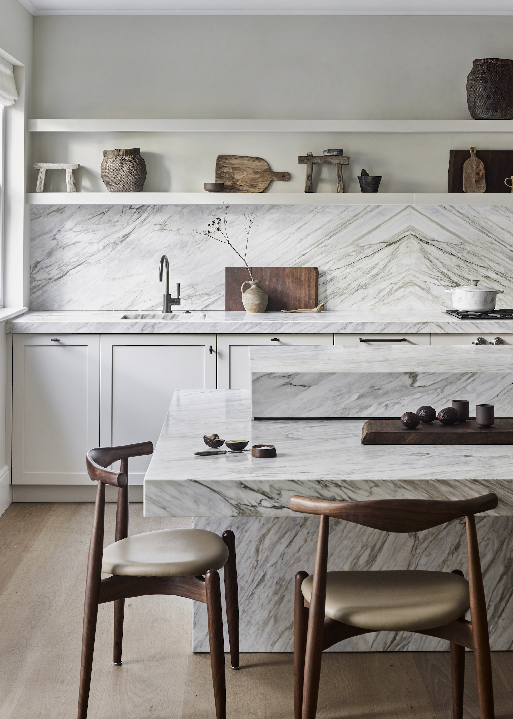 marble island with two wood dining chairs. On the island are wooded kitchen essentials.