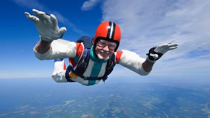 An older skydiver smiles as he freefalls.