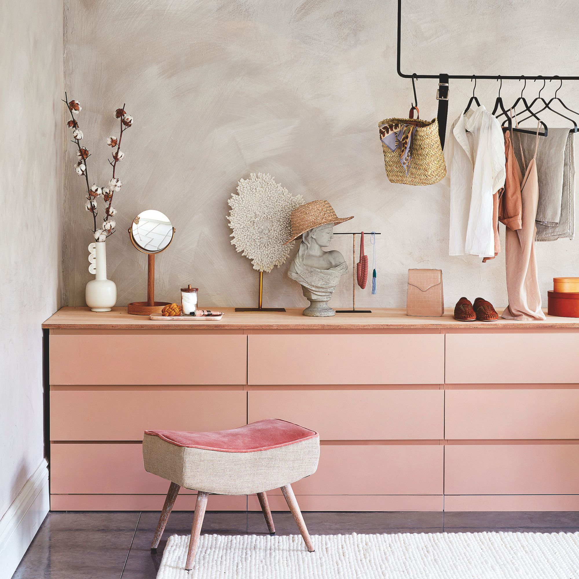 Dressing area with wide, pink drawers covered in accessories and a hanging rail above it