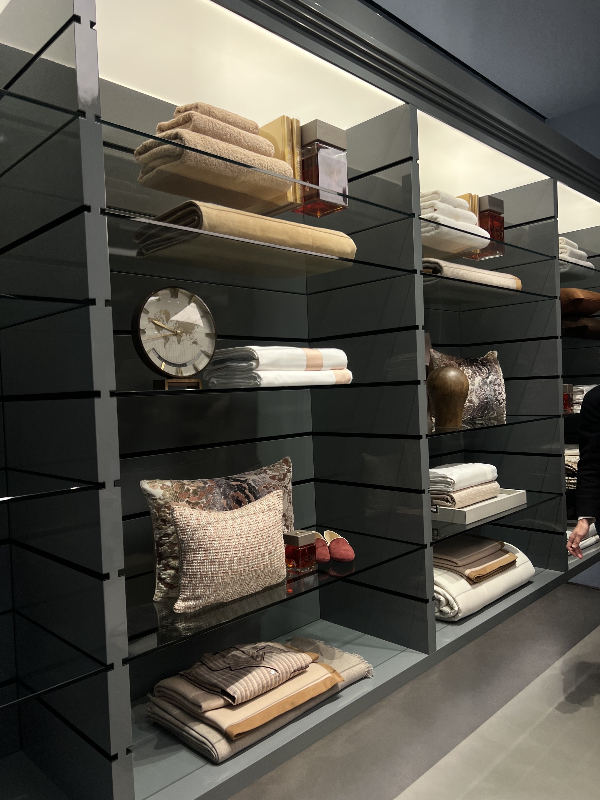 Image of a luxury bedding in a white and light pink colorway displayed on gray and glass shelving in a store.